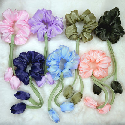 Pastel lavender scrunchies with two tulip buds and green stem ribbons, displayed on white fur background.