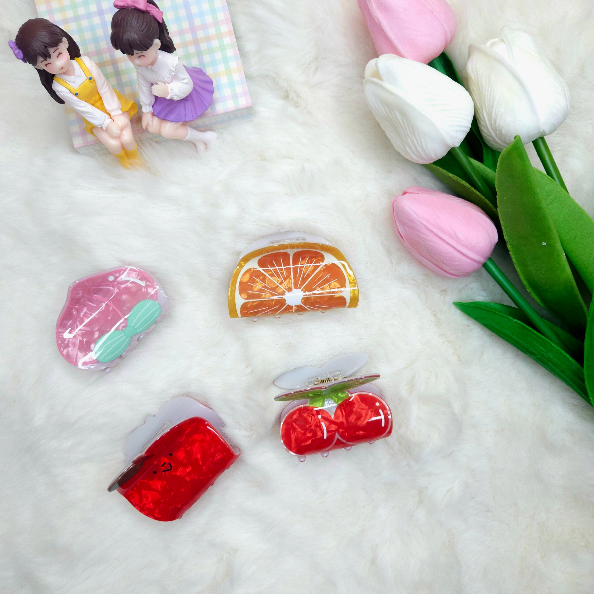 Colorful fruit-shaped hair clips on a textured surface with tulips in the background