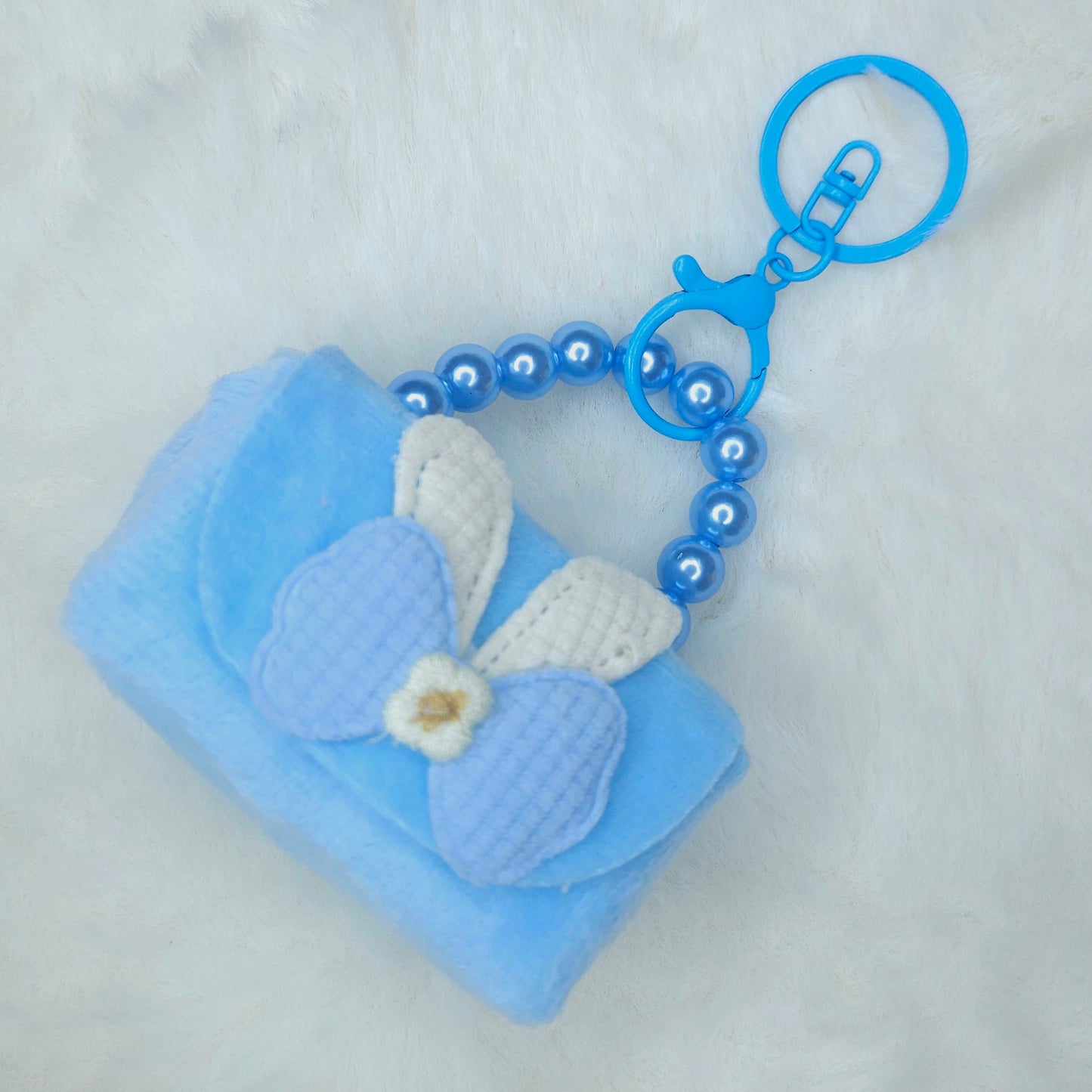 Blue keychain with a small pouch and decorative elements on a light gray background