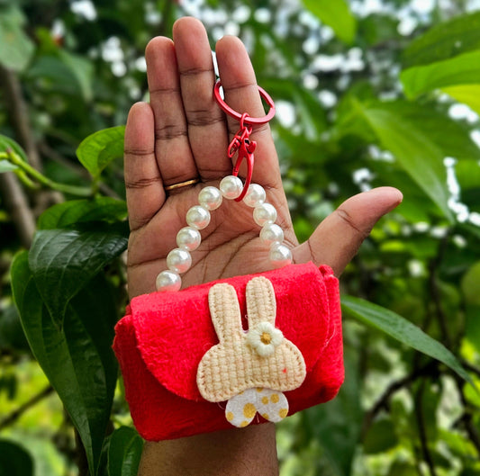Red pouch with bunny design and pearl strap held in a hand against a green leafy background