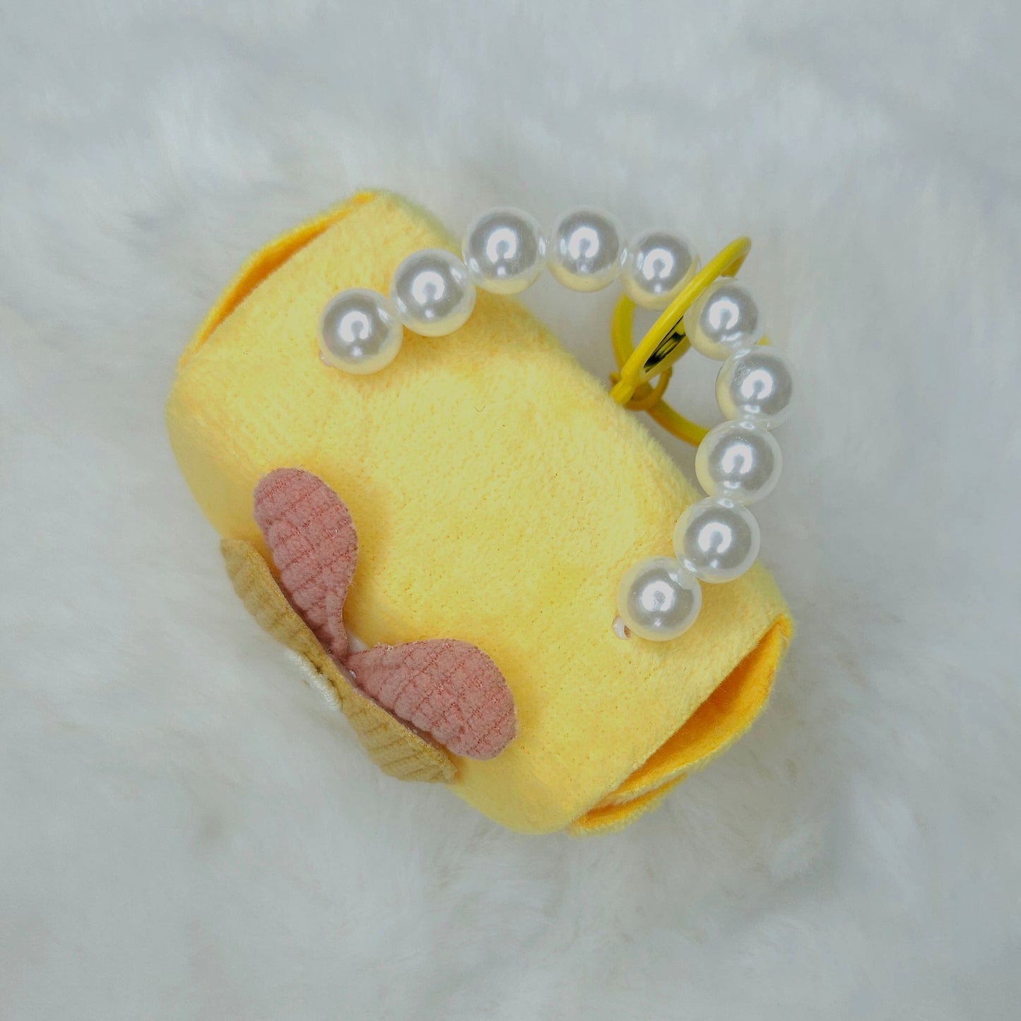 Yellow plush toy with pink bow and pearl-like beads on a white background